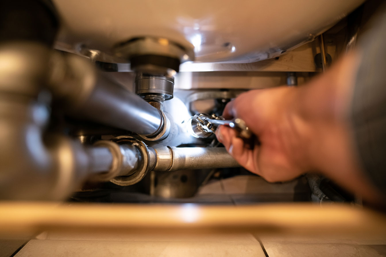 Plumber repairing pipes under a kitchen sink, tools spread on a towel